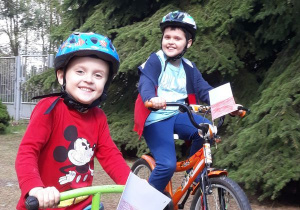 Dwóch chłopców jedzie na rowerach. Na głowach maja kaskia przy kierownicach przymocowane choragiewki biało - czerwone, wykonane samodzielnie.