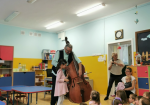 Dziewczynka z pomocą muzyka próbuje grać na instrumencie.