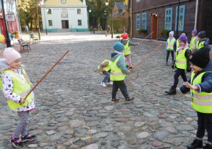 Dzieci na dziedzińcu muzeum bawią się w starodawne zabawy " kółko i kijek".