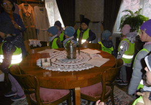 Dzieci przebywają w pomieszczeniu fabrykantów, okrągły drewniany stolik z chaftowaną serwetą