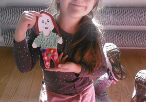 Dziewczynka trzyma lalkę z tektury w stroju zaprojektowanym prze siebie