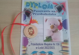 Na stoliku leży kolorowy dyplom i medal Pasowanie na Przedszkolaka.