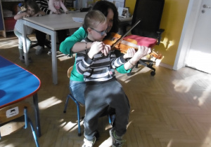 Skrzypaczka z chłopcem na kolanach gra na skrzypcach.