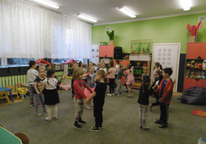 Dzieci z grupy 4 stoją w parach na dywanie w sali.