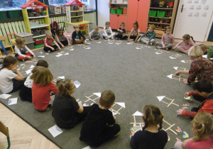 przedszkolaki siedzą na dywanie i układają z elementów szablon karmnika.