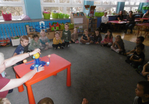 Dzieci z grupy 3 siedzą na dywanie, nauczycielka prezentuje krążenie planet wokół słońca.