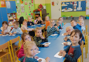 Dzieci siedzą przy stolikach i częstują się ciasteczkami.