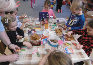 Dzieci z grupy 3 przy stolikach dekorują pierniczki świąteczne.