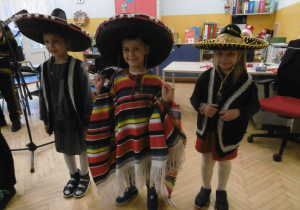 Troje dzieci prezentuje kolorowe stroje meksykańskie.