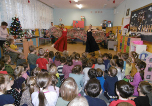 Przedszkolaki siedzą na dywanie, tańcerki w strojach hiszpańskich prezentują taniec.