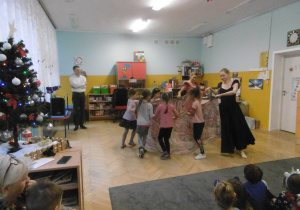 Kilkoro dziewczynek na środku sali z pomocą tancerki tańczą z chustą.