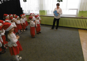Dzieci z grupy 1 w stojach mikołaja prezentują taniec w tle stoi nauczycielka