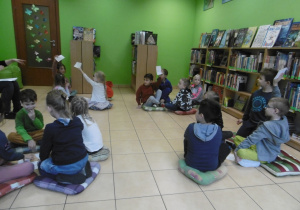 Dzieci w grupkach siedzą na podłodze i rozwiązują zadania proponowane przez panią bibliotekarkę.