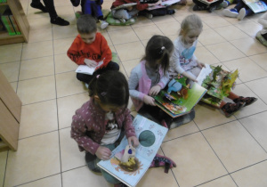 Przedsdzkolaki siedzą na podłodze i oglądają książki.
