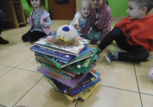 Dzieci odkładają książki tworząc piramide, na szczycie leży maskotka.