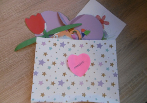 Kolorowa koperta z upominkami dla dziadków wykonanymi własnoręcznie przez dziecko: kwiatek, serduszko, filiżanka.