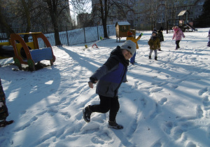 Dzieci w ogrodzie przedszkolnym bawią się na śniegu.