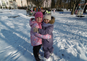 Dziewczynki przytulają się do siebie. W tle ogród przedszkolny w zimowej szacie.