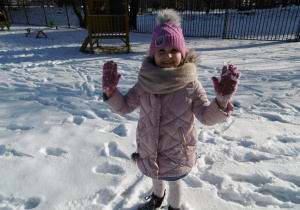 Dziewczynka stoi i pokazuje ośnieżone rękawiczki