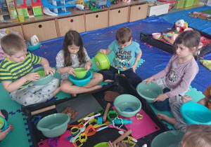 Dzieci siedza na rozłożonych ceratach. Kazde dziecko robi własne kolorowe ciasto