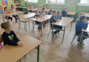 Przedszkolaki siedzą w ławkach w sali lekcyjnej