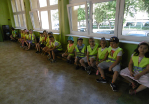 Dzieci siedzą na ławkach gimnastycznych stojących na korytarzu 3