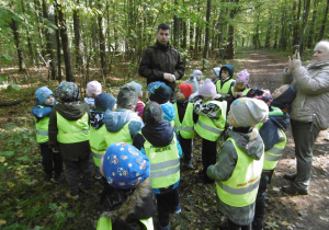 Pan leśniczy wraz z grupą dzieci stoją na leśnej ścieżce i obserwują przyrodę.