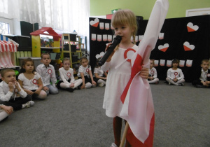 Dziewczynka z grupy II recytuje wiersz na konkurs, w ręce trzyma flagę Polski