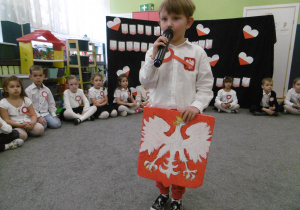 Chłopic z grupy II recytuje wiersz na konkurs, w ręce trzyma godło Polski