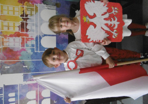 Chłopiec trzyma flag Polski, dziewczynka trzyma godło Polski.