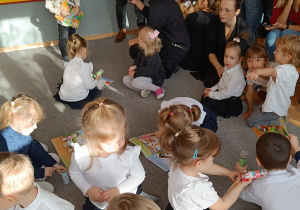 Dzieci siedzą na dywanie i oglądają książeczki-pamiątki pasowania