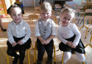 Troje dzieci po pasowaniu dumnie siedzi na przedszkolnych krzesełkach