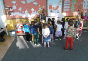 Nauczycielka stoi przy tablicy na której dziecko układa obrazek z części.