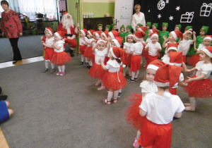 Maluszki tańczą świąteczny taniec. W tle siedzi Mikołaj i stoją nauczycielki grup.