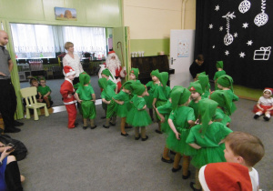Dzieci-elfy tańczą świąteczny taniec. W tle siedzi Mikołaj, stoją nauczycielki grup i animator tańca.