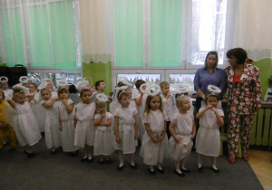 Dzieci-aniołki stoją na scenie. W tle stoi nauczycielka grupy i pani dyrektor przedszkola.
