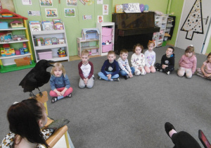 Dzieci z grupy II siedzą na dywanie i słuchają krakania kruka.