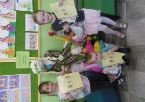 Dwie dziewczyni i jeden chłopiec - laureaci konkursu, stoją przy kukłach marzanny, w dłoniach trzymają dyplomy i nagrody.