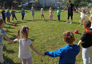 Przedszkolaki stoją na polance w kole.