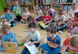 Dzieci siedzą na poduszkach i oglądają wybrane książki.