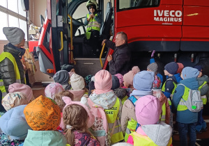 Przedszkolak w kasku strażackim stoi w szoferce samochodu strażackiego.