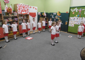 Dziewczynka na tle grupy zaprasza do wspólnego odśpiewania hymnu Polski