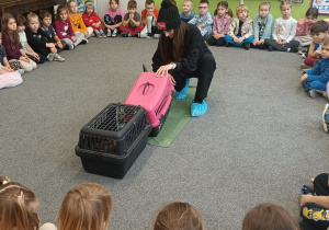 Dzieci siedzą w kole. Na środku stoją dwie klatki z zwierzętami.