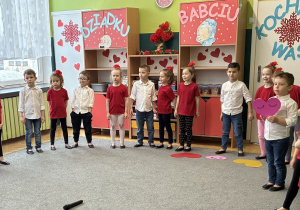 Grupa dzieci stoi w półkolu na scenie.