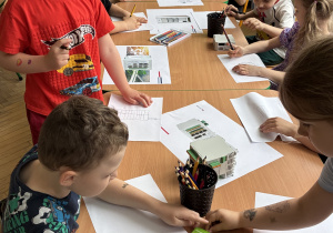 Dzieci siedzą przy stolikach i rysują na temat obejrzanej prezentacji.